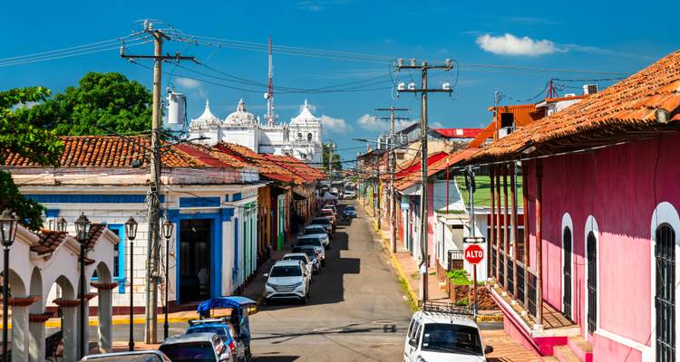 Colorful colonial street with cars and a cathedral in the background.