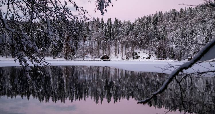 Paysage enneigé serein avec un lac reflétant et une forêt.