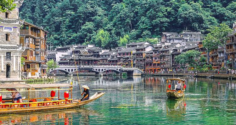 Traditional Chinese architecture along a river with boats in Fenghuang.