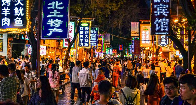 A crowded street market with people and colorful signs.