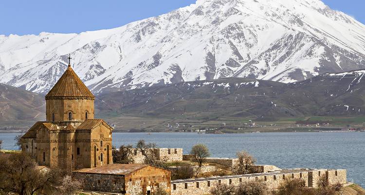 Historic church by a lake with snowy mountains.