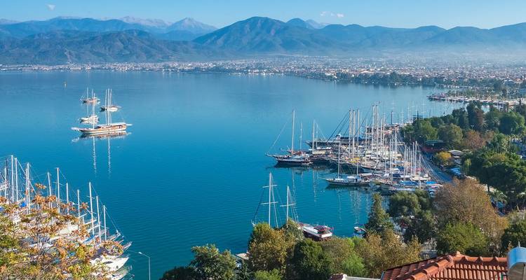 Luftaufnahme über einen mit Yachten gefüllten Hafen und eine blaue Bucht mit Bergen im Hintergrund in der Nähe von Fethiye