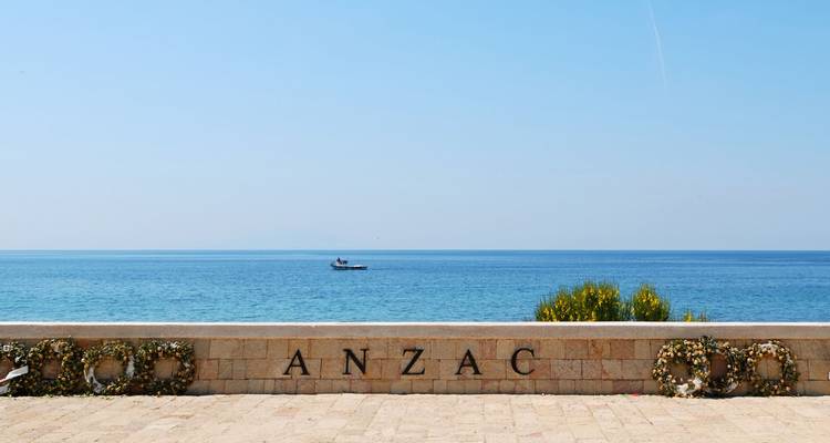 Einfache Gedenkwand am Meer mit der Aufschrift ANZAC und Kränzen mit Blick auf das ruhige, blaue Ägäische Meer