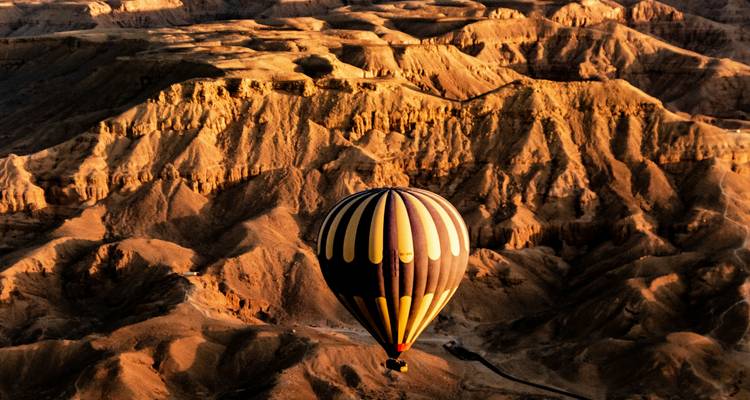 Globo aerostático volando sobre terreno desértico al atardecer.