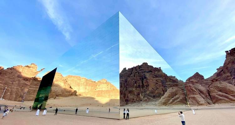 Structure cubique réfléchissante dans le désert avec des personnes autour.