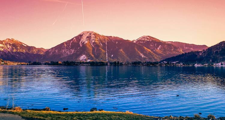 Un lago sereno con montañas en la distancia, bajo un cielo rosado.