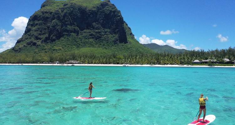 Des pratiquants de paddle sur un océan bleu clair avec une montagne en arrière-plan.