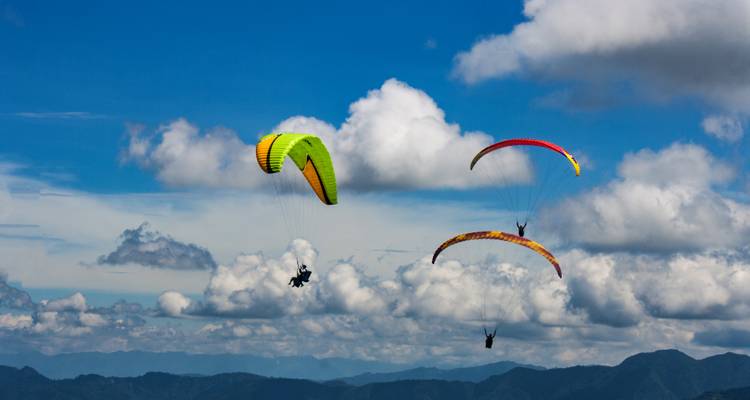 Des parapentistes volant au milieu des nuages au-dessus d'un terrain montagneux.