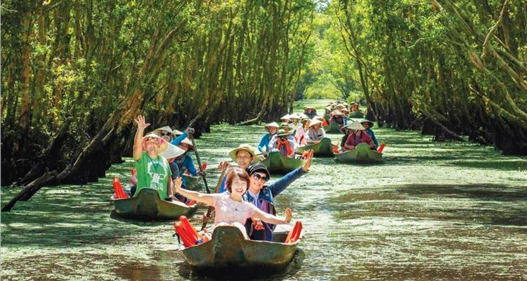 Turistas en embarcaciones tradicionales navegando por un canal frondoso.