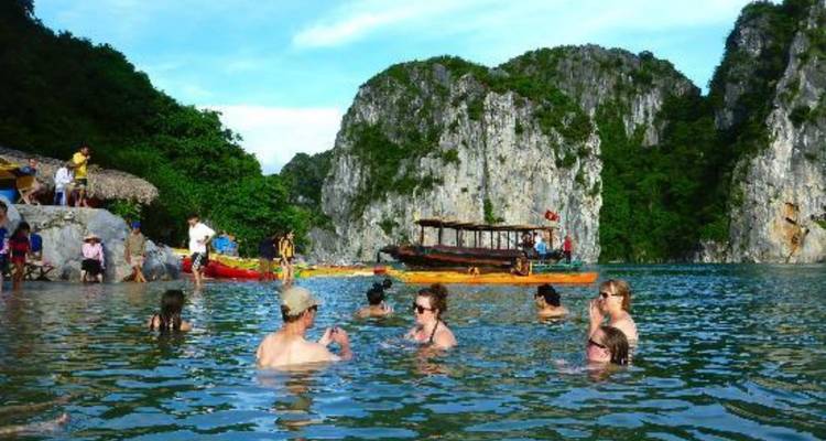 Turistas nadando en agua cristalina con acantilados de piedra caliza al fondo.