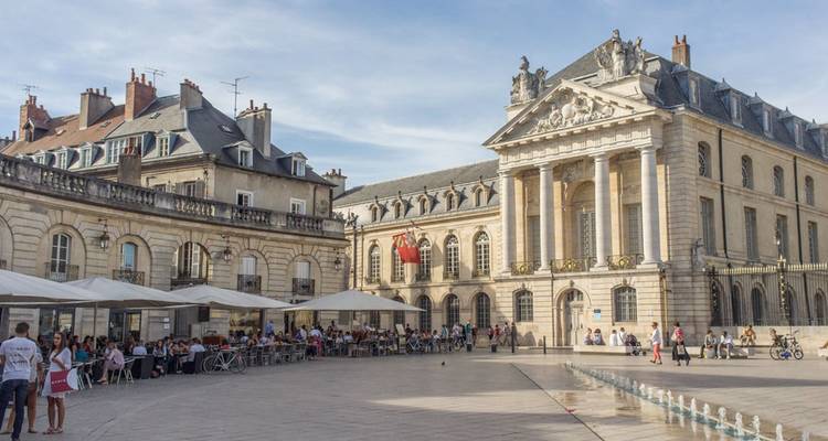 Place de ville ouverte avec bâtiments historiques et terrasses de café.