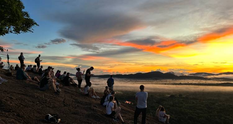 Des gens rassemblés sur une colline regardant un coucher de soleil éclatant.