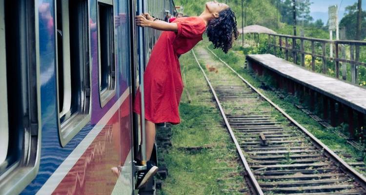 Personne se penchant hors d'un train traversant une végétation luxuriante.