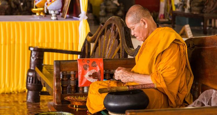 Monk sitting and crafting in a temple area.
