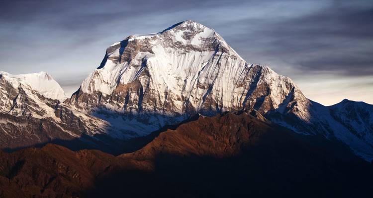 Una majestuosa cima montañosa con nieve que refleja tonos rosados al atardecer.