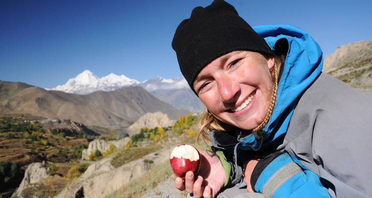 Una persona sonriente disfrutando de una manzana con montañas de fondo.