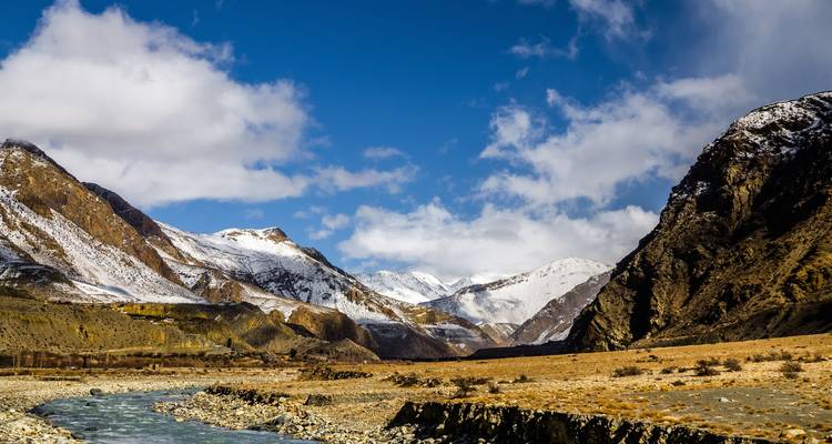 Una vista amplia y pintoresca de un valle fluvial con montañas cubiertas de nieve.