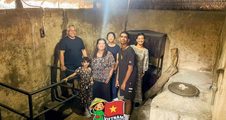Un groupe familial se tient à l'intérieur d'un bunker souterrain historique ; un autocollant de dessin animé du Vietnam est superposé.