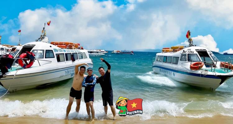 Trois amis posent sur une plage à côté de bateaux rapides ; filigrane cartoon Vietnam présent.
