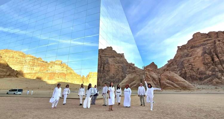 Group in white standing in front of a mirrored building in a desert landscape.
