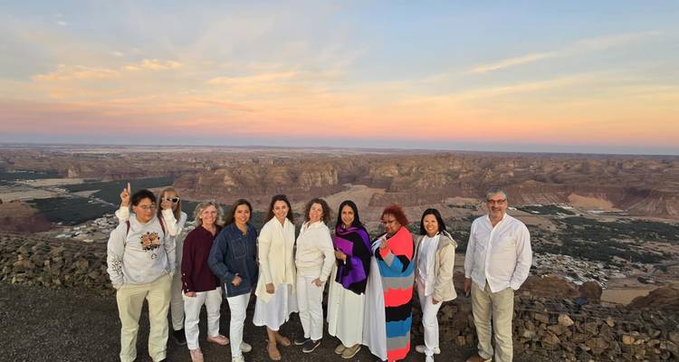 Group of tourists in white and colorful outfits overlooking a canyon at sunset.