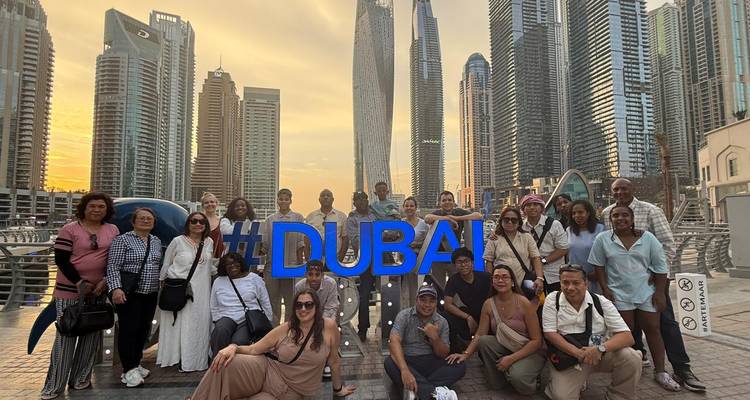 Group with #DUBAI sign and skyscrapers at sunset.
