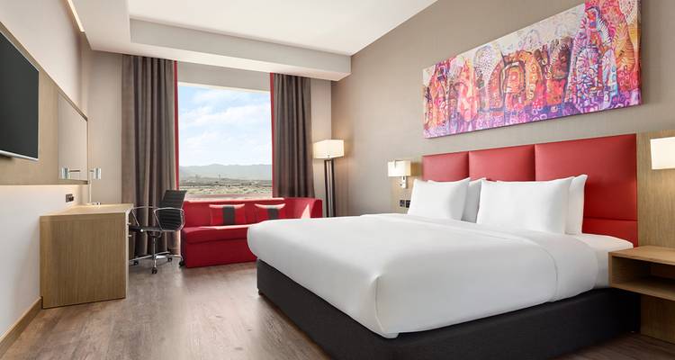 Chambre d'hôtel avec un grand lit, une œuvre d'art au-dessus du lit, et une vue par la fenêtre.