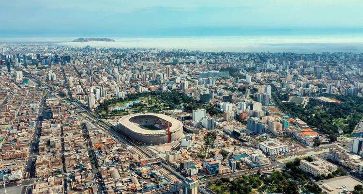 Vue aérienne d'un stade dans une zone densément construite, entouré de verdure.