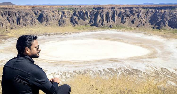 Personne assise près d'un grand cratère ou d'une formation géologique.