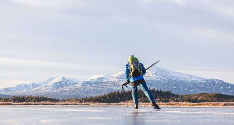 Personne faisant du patin à glace sur un lac gelé avec des montagnes en arrière-plan.