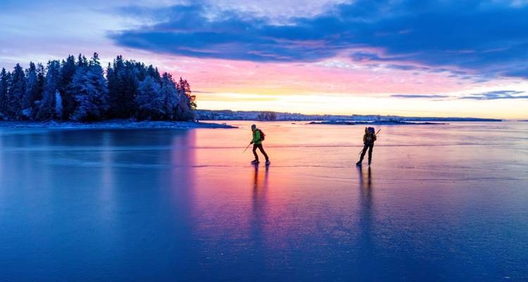 Deux personnes patinant sur un lac pendant un coucher de soleil coloré.