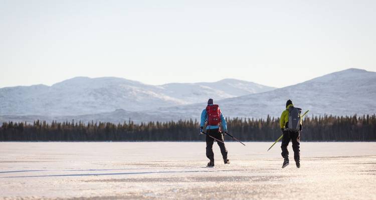 Deux personnes patinant sur un paysage gelé expansif avec des montagnes.