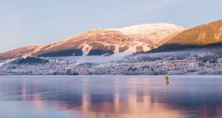 Personne patinant sur un lac gelé avec une ville enneigée and des montagnes.