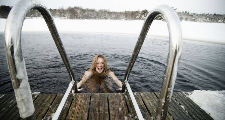 Personne dans l'eau glacée grimpant sur un quai couvert de neige.
