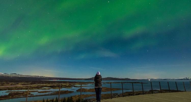 Une personne observant les aurores boréales au-dessus d'un vaste paysage.