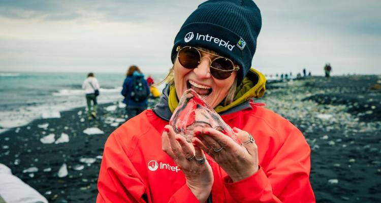 Personne tenant un morceau de glace transparente sur une plage de sable noir.