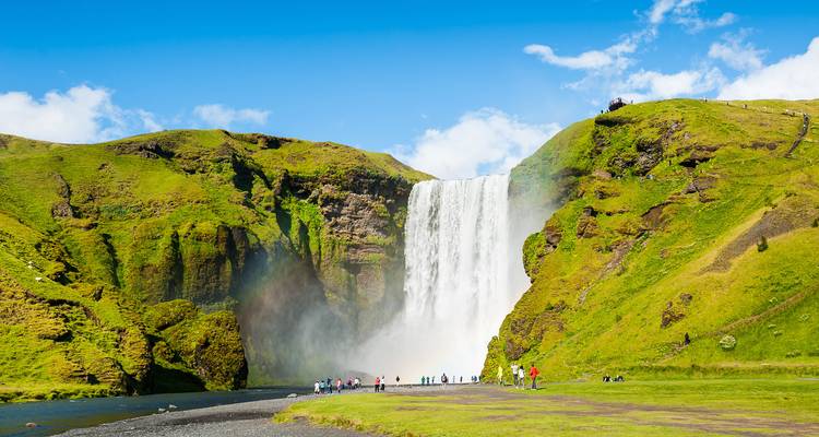 Des gens près d'une grande cascade par une journée ensoleillée.