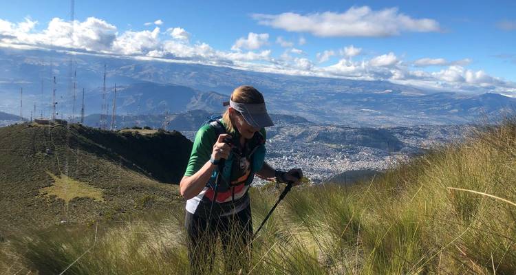 Wanderer mit Trekkingstöcken auf einem grasbewachsenen Hügelhang mit Panoramablick.