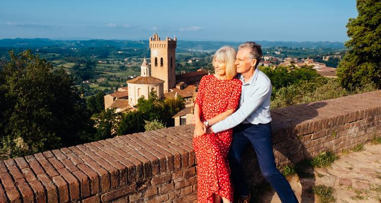 Couple embracing by a stone wall overlooking the countryside.