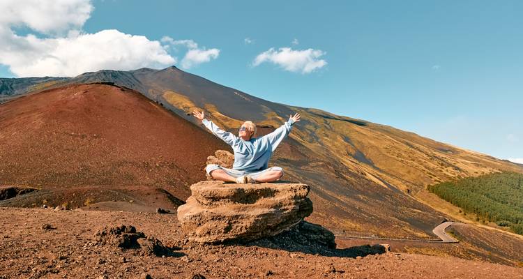 Person meditating on a rocky outcrop in a volcanic landscape under a clear sky.