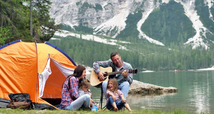 Family with tent by a lakeside, mountains in the background.