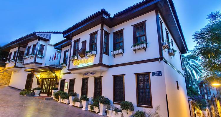 Buitenkant van een boetiekhotel in de schemering, met een bord en potplanten.