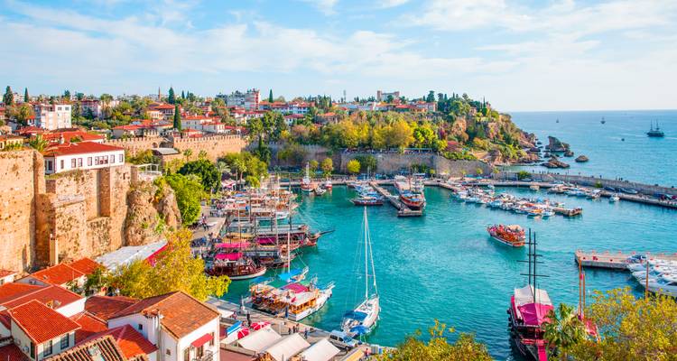 Colorful boats moored in Antalya’s historic Kaleici harbour surrounded by stone walls and old town buildings.