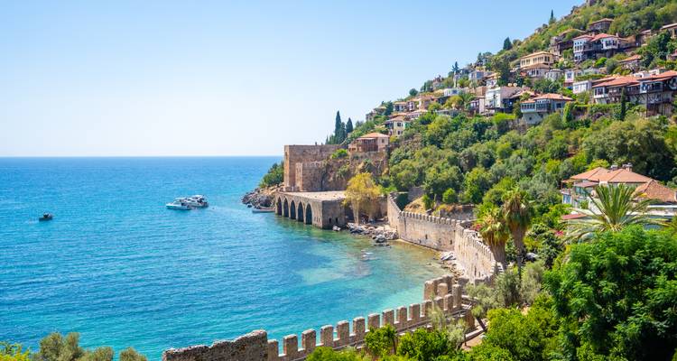 Turquoise bay with medieval walls and arched shipyard of Alanya beneath a hillside of colorful houses.
