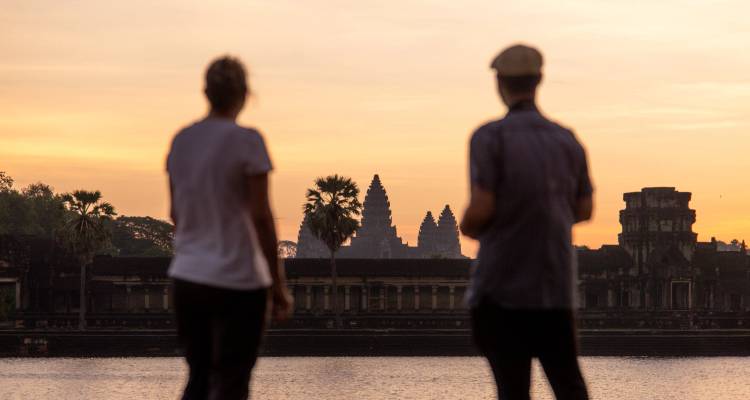 Silhouettierte Reisende bewundern Angkor Wat über den Wassergraben hinweg bei Sonnenaufgang.