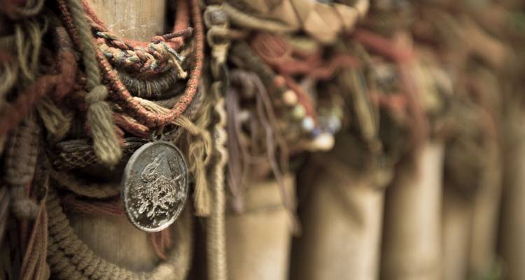 Nahaufnahme von bunten Erinnerungsbändern und einer abgenutzten Medaille, die an Bambusstangen hängen.