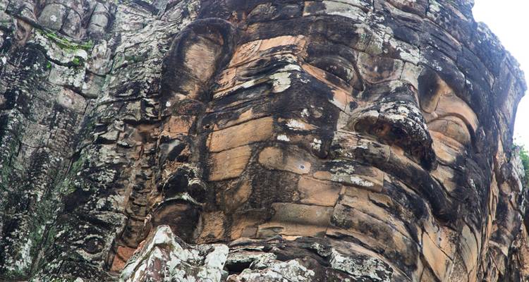 Verwittertes Sandsteinfries einer Bayon-Tempelskulptur, das aus dunklem, flechtenbedecktem Gestein hervortritt.