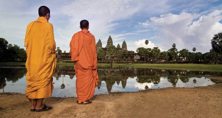 Dos monjes budistas con túnicas azafrán de pie junto al estanque de reflexión mirando hacia Angkor Wat al otro lado del agua.