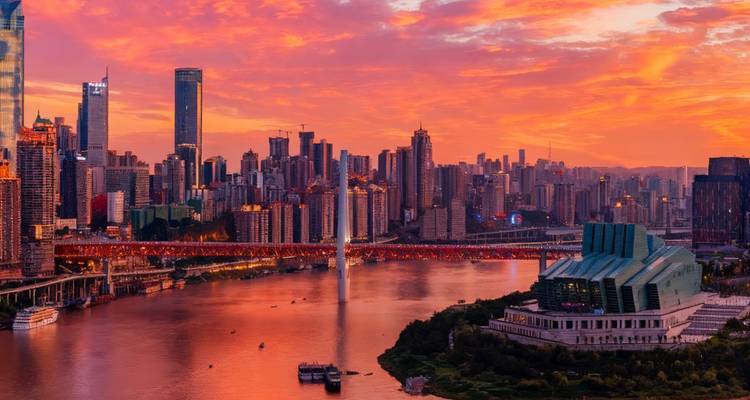 Cityscape of Chongqing with river and buildings at sunset.