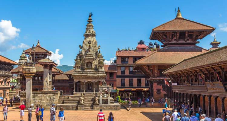 Des gens se promènent autour d'une place historique avec des temples et une architecture néwaraise traditionnelle.